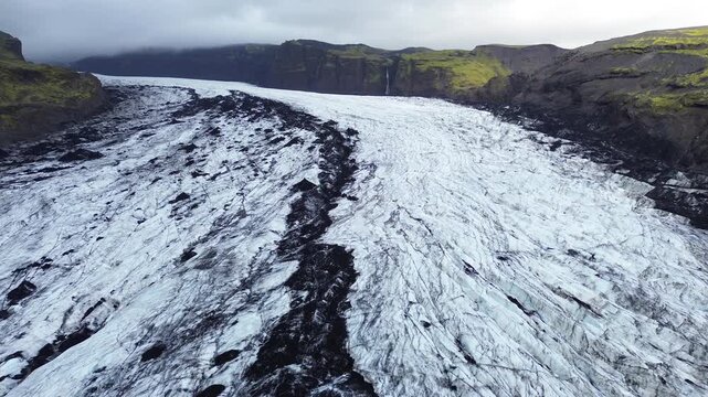 Aerial view of a glacier tongue with textures of ice and black volcanic ash