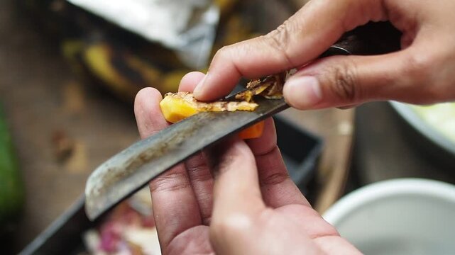 Close-up of hands carefully peeling a fresh turmeric root with a knife, preparing it for cooking or culinary use.