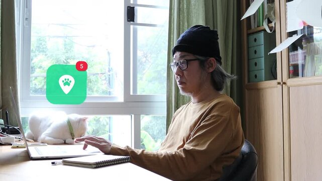 Mature Asian man with white hair using laptop at home office next to his cat, featuring a 3D tracked pet paw location pin map pointer notification pop up and red counter.