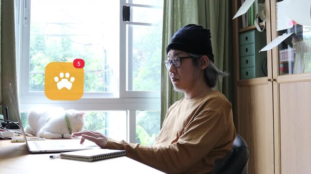 White haired mature Asian man using laptop at home with his cat, showing a 3D tracked animal paw footprint veterinary care notification pop up and red counter.