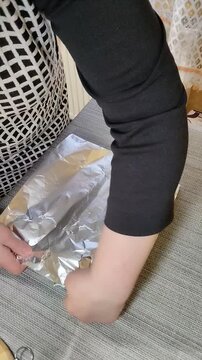 Woman's hands wrapping marinated pork meat with spices in aluminum foil for baking, Preparing homemade roasted meat roll with seasoning on the table close-up.