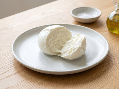 Fresh mozzarella cheese ball torn in half on a white plate