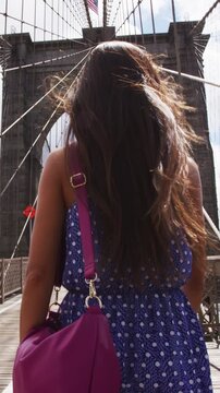 New York City Woman. Young woman portrait on Brooklyn bridge, New York city NYC, Manhattan, USA. Walking tourist in blue dress doing summer travel by landmark. VERTICAL VIDEO SLOW MOTION