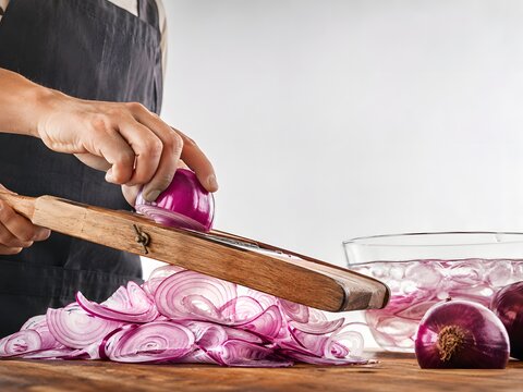 Close up of cook hands slicing fresh raw red onion using traditional wooden mandoline slicer tool