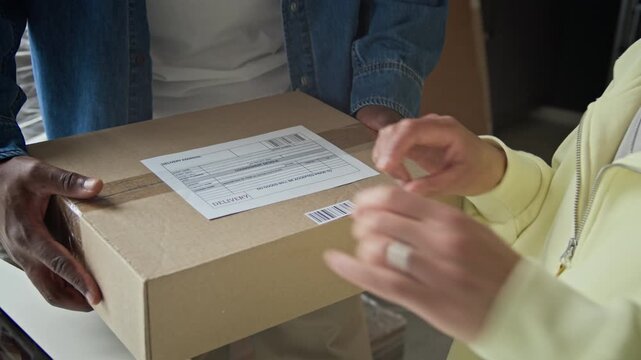 Handheld shot of African American man delivering cardboard box to woman scanning barcode with handheld scanner. Footage ideal for e-commerce, logistics, and supply chain marketing