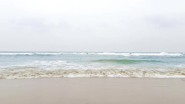 Bright ocean waves gently washing over a sandy tropical beach in sunlight, peaceful coastal seascape with turquoise water, white sea foam and relaxing summer vacation atmosphere in 4K slow motion