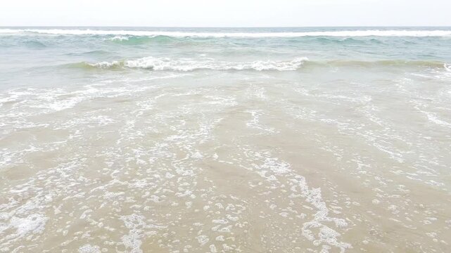 Bright ocean waves gently washing over a sandy tropical beach in sunlight, peaceful coastal seascape with turquoise water, white sea foam and relaxing summer vacation atmosphere in 4K slow motion