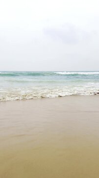 Bright ocean waves gently washing over a sandy tropical beach in sunlight, peaceful coastal seascape with turquoise water, white sea foam and relaxing summer vacation atmosphere in 4K slow motion