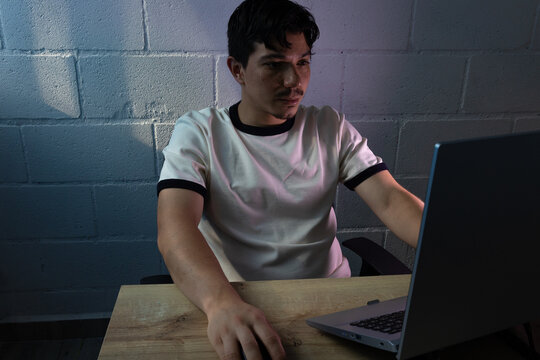 Focused man working from home at night. The computer screen illuminates his face in a dark environment, reflecting productivity, dedication, and remote work