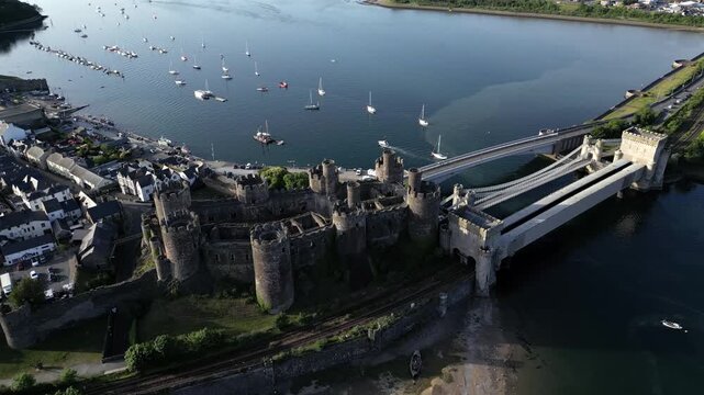 Witness Conwy Castle from above as it stands proudly beside the water. The surrounding area includes boats and a bridge, showcasing the historical site and its landscape in detail
