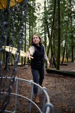 Woman throws frisbee at disc golf course in forest setting
