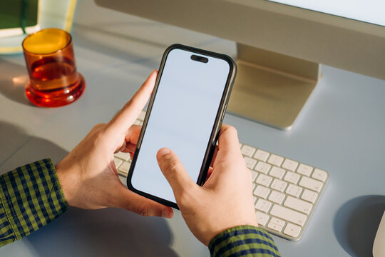 The man uses a computer and a mobile phone with a white screen