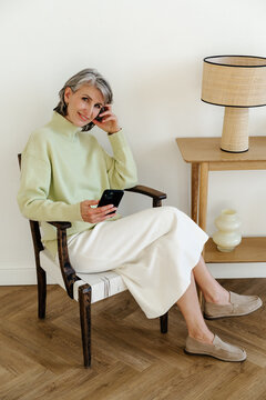 Smiling Mature Woman Relaxing with Smartphone in Cozy Interior