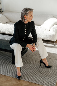 Stylish Mature Woman Sitting on Table in Elegant Black Blazer Indoors