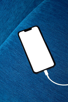 Smartphone with white blank screen charging on blue fabric