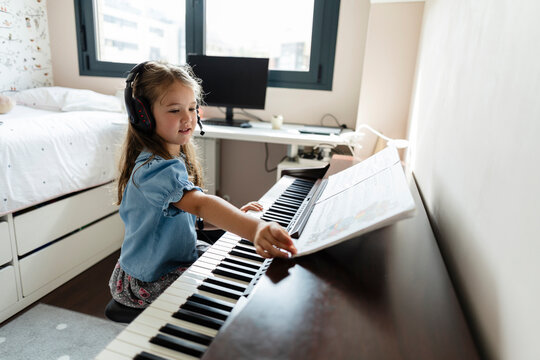 Young girl learning piano with headphones in her bedroom