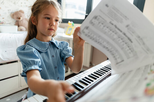 Young girl learning piano with music sheet in room