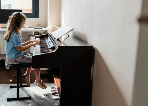 Young girl learning playing digital piano with headphones