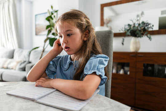 Young girl thinking while doing homework at home
