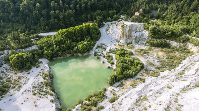 Aerial view of Kamnolom Plese pri Skofljici featuring a turquoise pond surrounded by white stone cliffs and lush green forest in Mali Vrh pri Smarju, Grosuplje, Slovenia.