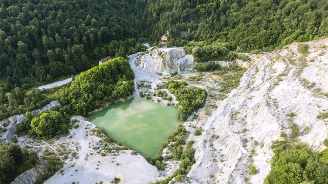 Aerial view of Kamnolom Plese pri Skofljici featuring a vibrant green pond surrounded by white limestone cliffs and dense forest in Mali Vrh pri Smarju, Grosuplje, Slovenia.