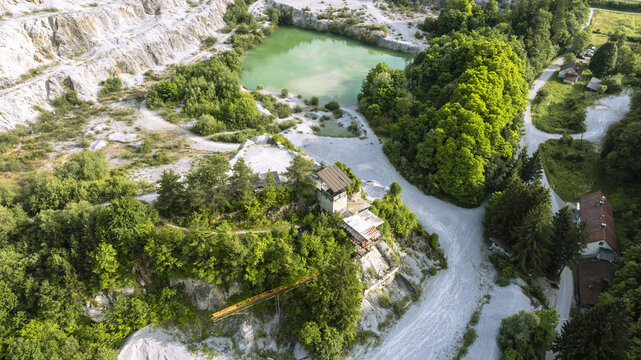 Aerial view of Kamnolom Plese pri Skofljici quarry with a turquoise pond, rocky cliffs, dense forest, and industrial structures in Mali Vrh pri Smarju, Grosuplje, Slovenia.