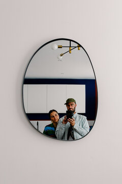 Mirror selfie of a photographer holding a camera in a modern kitchen