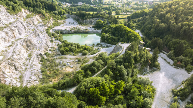Aerial view of Kamnolom Plese pri Skofljici quarry with a vibrant green pond surrounded by dense forest and rocky terrain in Mali Vrh pri Smarju, Grosuplje, Slovenia.