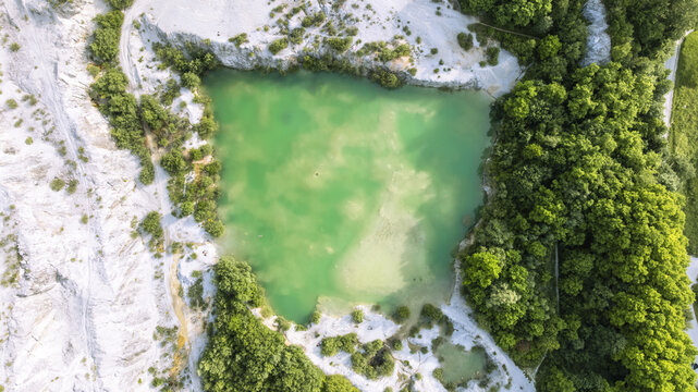 Aerial view of turquoise water in the Kamnolom Plese pri Skofljici quarry surrounded by lush green forests and white rocky cliffs in Mali Vrh pri Smarju, Grosuplje, Slovenia.