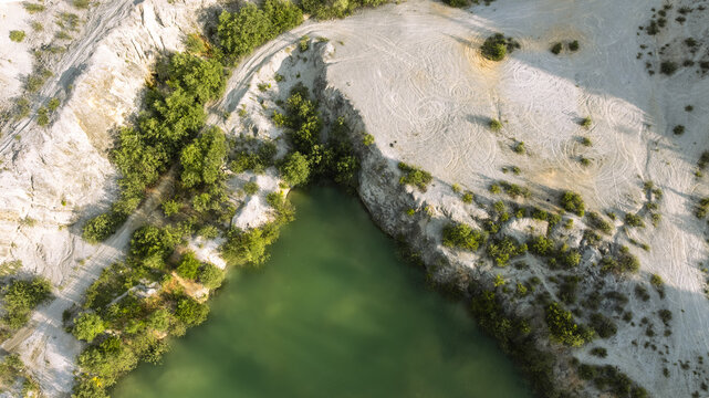 Aerial view of Kamnolom Plese pri Skofljici featuring a green quarry lake surrounded by rocky cliffs and sparse vegetation in Mali Vrh pri Smarju, Grosuplje, Slovenia.
