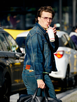 Man Drinks From a Cup While Walking on a Busy Street