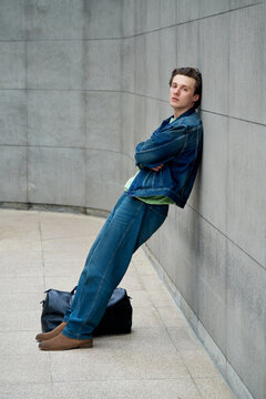 Young Man Leans Against Wall With Bag in Urban Area