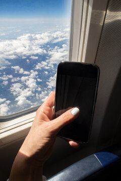 Airplane window blue sky with clouds and mobile phone in hand closeup