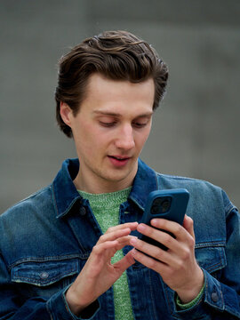 Young Man Uses Smartphone While Standing in Urban Area