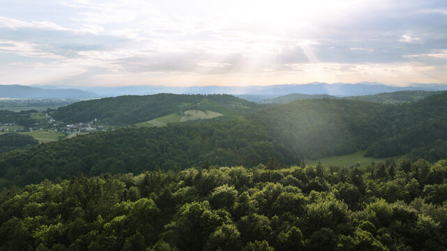 Aerial view of lush green forests and rolling hills under a bright sunlit sky in Mali Vrh pri Smarju, Grosuplje, Slovenia.