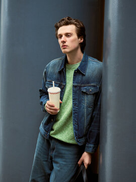 Young Man Enjoys Drink While Leaning Against Wall in City