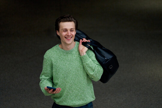 Man Carrying Bag Walks While Using Phone in Public Space