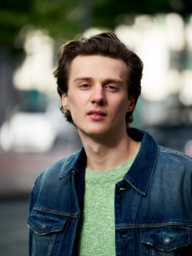 Young Man Stands in City Street Wearing Denim Jacket and Sweater