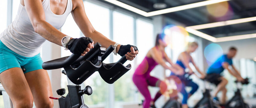 Woman gripping the handlebars of a stationary exercise bike during a spinning class in bright gym.