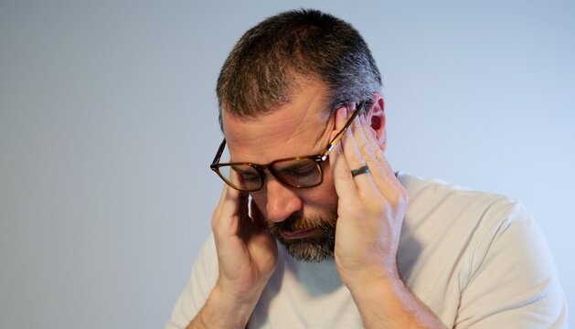 Exhausted adult man with glasses rubbing temples and forehead while dealing with severe headache, psychological pressure, mental stress, or anxiety