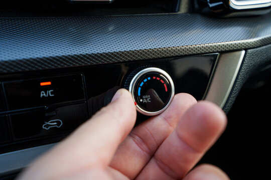 Man hand adjusting temperature on car air conditioner, driver turning on vehicle climate control system during road trip