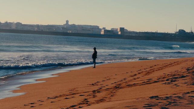 Man enjoying Atlantic Ocean view at sunset beach.

Relaxed travel lifestyle moment of a man standing near the shoreline and appreciating coastal scenery and ocean atmosphere.