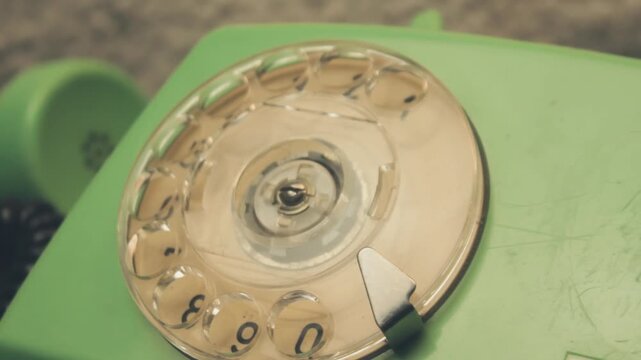 Extreme close-up finger rotating plastic dial of vintage rotary telephone. Mechanism turns, illustrating analog communication technology and dialing methods from the last century