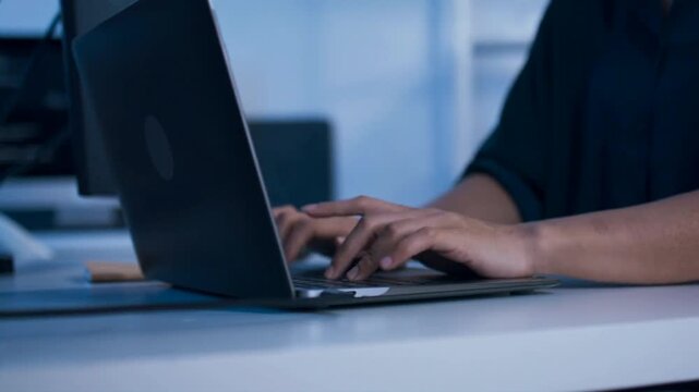 Professional worker typing on laptop keyboard in corporate office setting Close up profile view of hands working on computer laptop on office desk