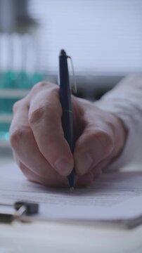 Hand of laboratory scientist writing medical test results or clinical research data on official document at desk. Vertical close up shot