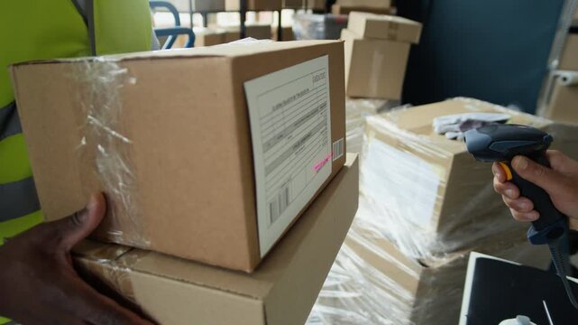 Cropped shot of African American worker holding cardboard boxes with colleague scanning barcode label using handheld scanner. Clip is ideal for logistics, supply chain, and e-commerce videos