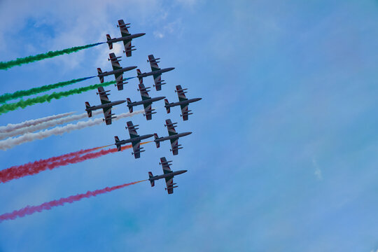 Italy , Aerobatic jet team performing precision formation flight. High-speed military aircraft trailing colored smoke during airshow demonstration.