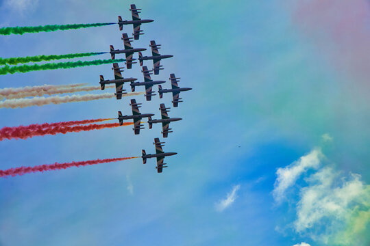 Italy , Aerobatic jet team performing precision formation flight. High-speed military aircraft trailing colored smoke during airshow demonstration.