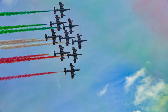 Italy , Aerobatic jet team performing precision formation flight. High-speed military aircraft trailing colored smoke during airshow demonstration.