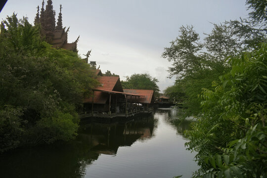 traditional wooden temple building with intricate carvings sits along a calm    lake, surrounded by lush green trees and reflection on the water surface under an overcast sky